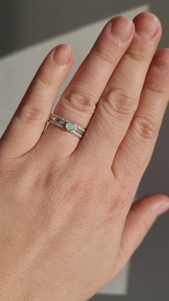 Close-up video of a hand wearing the Crystal Opal Silver Stack Ring Set in sunlight, highlighting the opal's unique transparency and kaleidoscope of colours against the textured Silver bands.