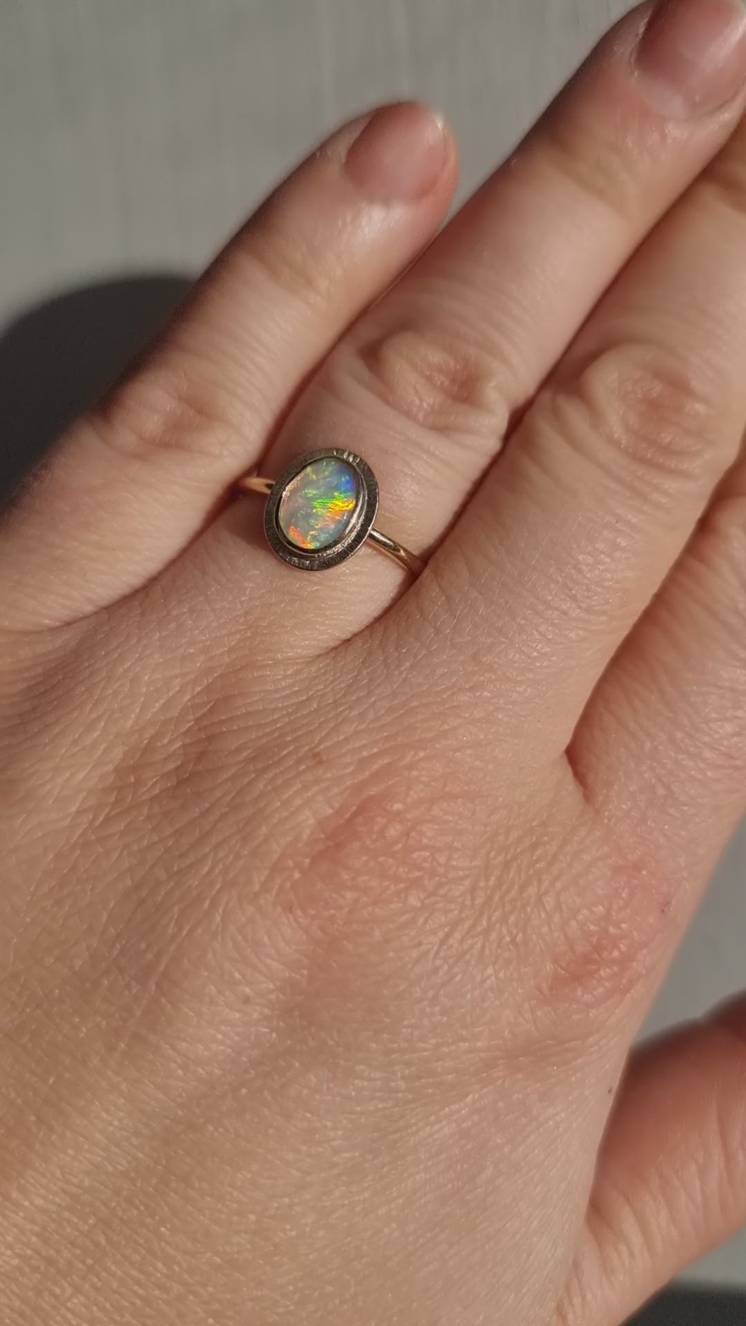 Close-up video of the Aura Gold Oval Crystal Opal Ring worn on a hand in sunlight, showcasing the opal's ethereal quality, unique transparency, and kaleidoscope of colours