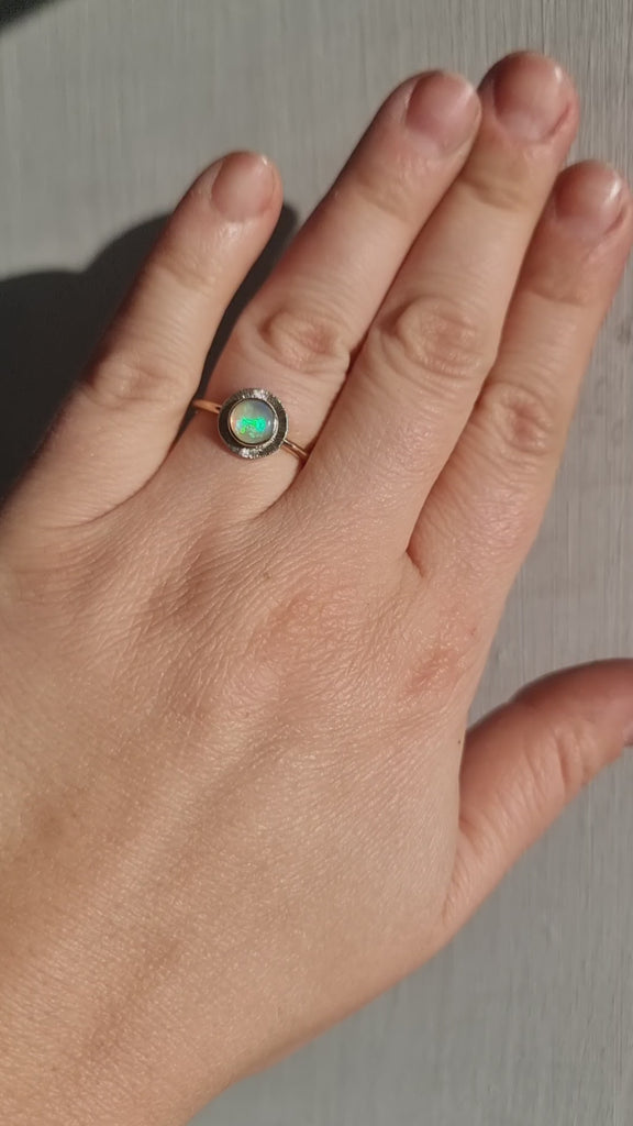 A gold ring featuring a multi-coloured Australian Crystal Opal set in a radiant gold engraved setting being worn on hand in the sunlight 